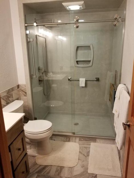 A bathroom with a toilet , sink and shower with a sliding glass door.