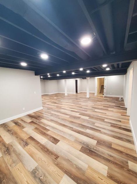 A large empty basement with wooden floors and a blue ceiling.