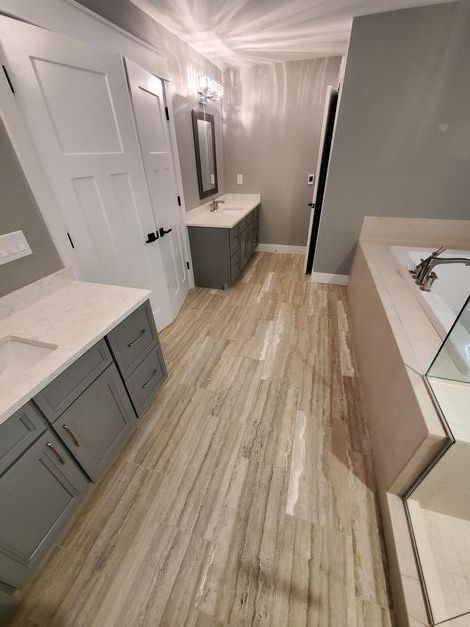 A bathroom with hardwood floors , gray cabinets , a sink and a mirror.