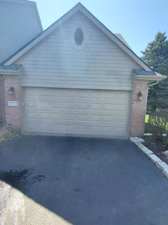 A white garage door is sitting in front of a brick house.