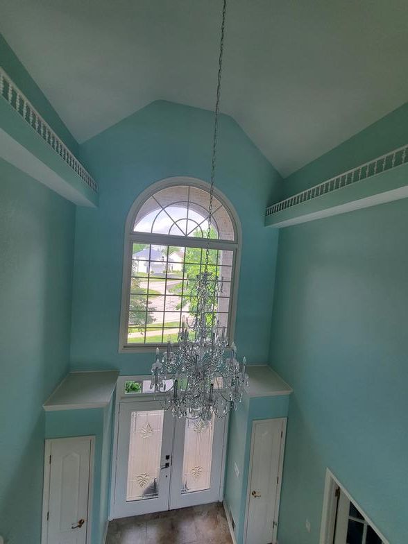 A hallway with a chandelier hanging from the ceiling and a large window.