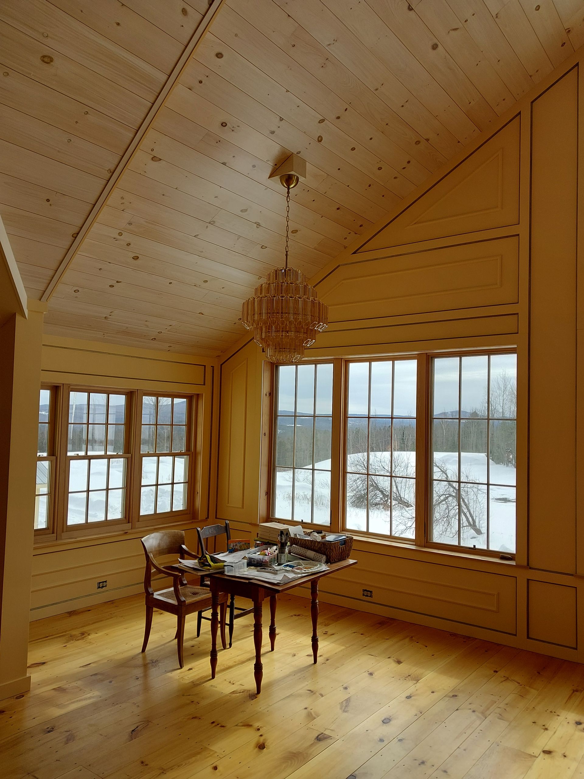 Cozy wooden dining room with chandelier, table, and large windows overlooking snowy landscape