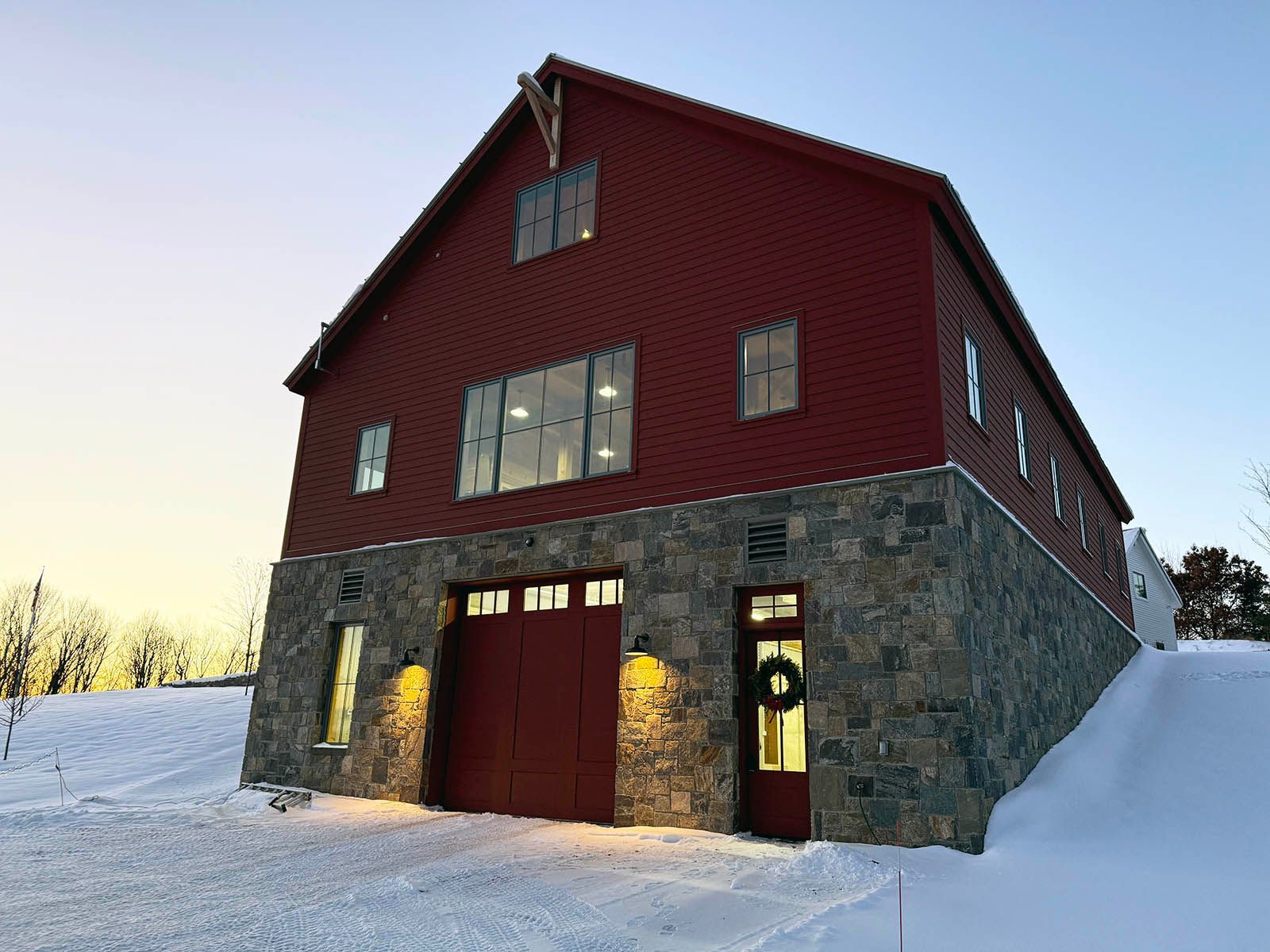 Red barn-style building with stone lower level and snowy surroundings at dusk
