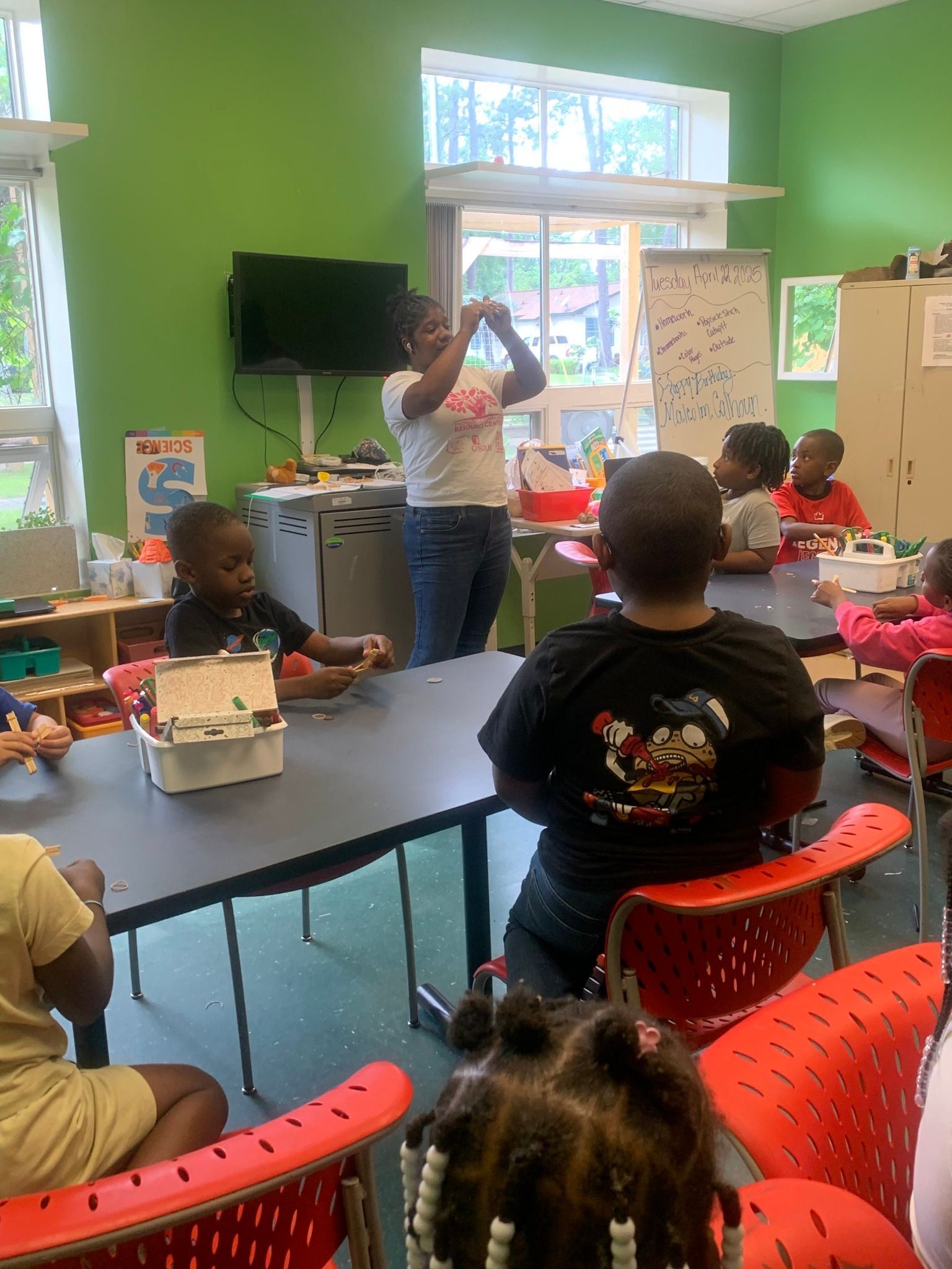 Wrestler in gray singlet celebrates victory, arms raised, opponent on mat. Arena crowd in background.