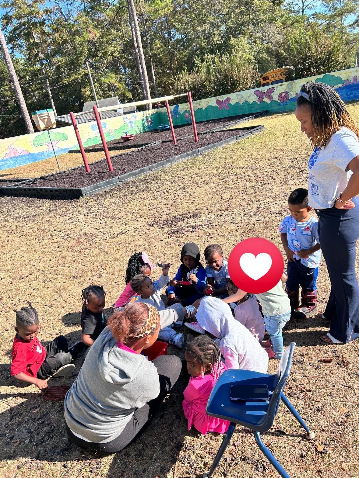 A group of children and adults sitting in a circle on a playground during an outdoor activity.