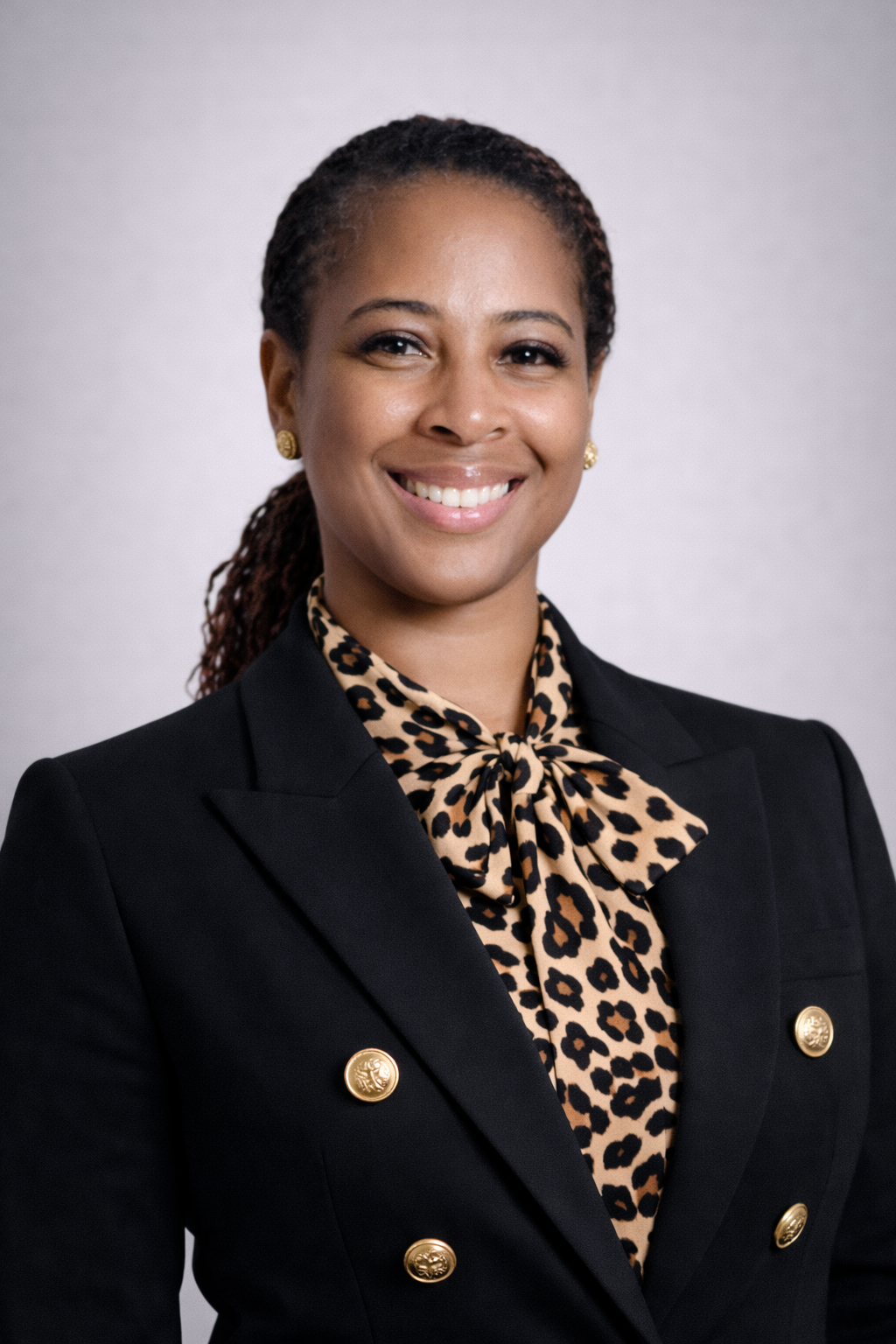 Man in a blue shirt standing outdoors, smiling. Background features greenery, fence.