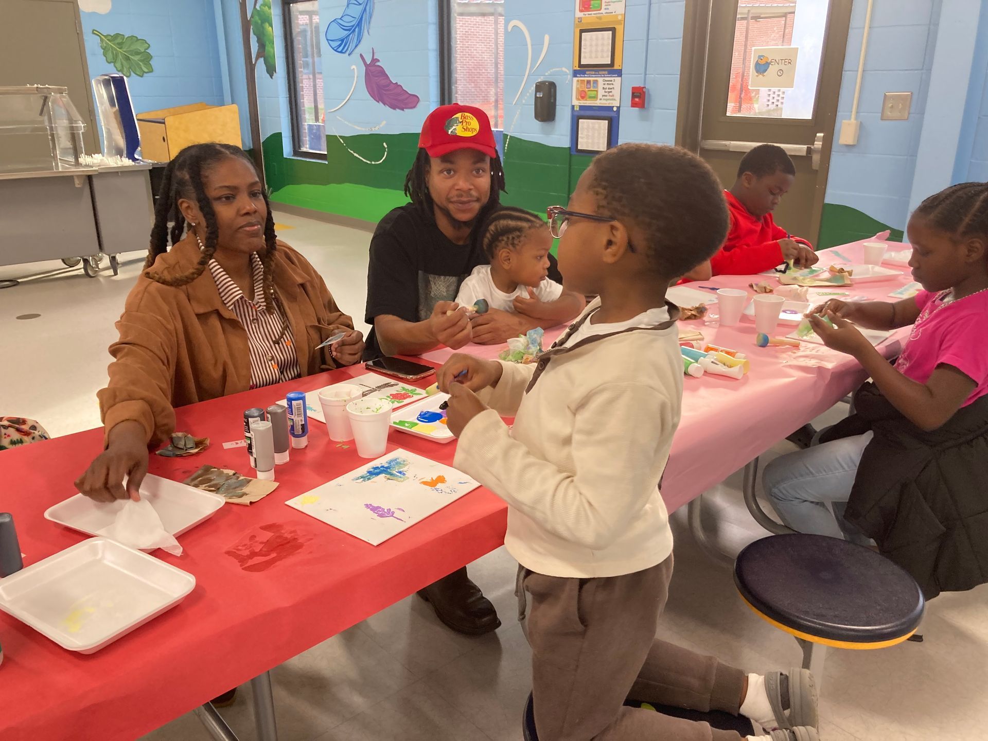 People at a red-covered table engaged in an arts and crafts activity in a brightly decorated community room.