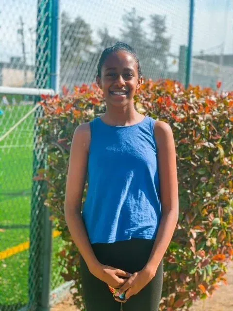 Woman in blue tank top smiles in front of green and brown background.