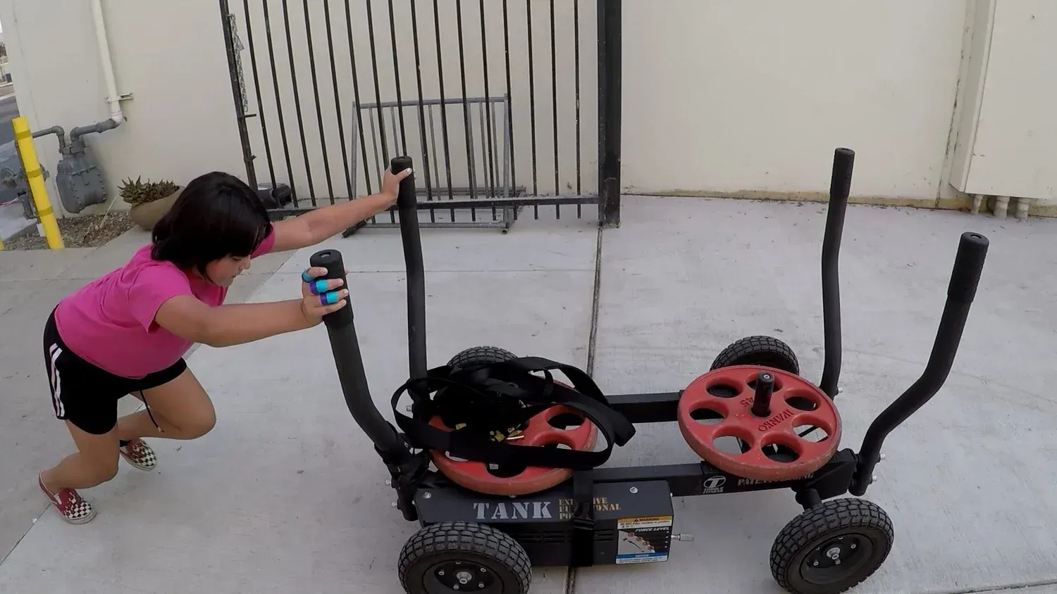 Girl pushing a black fitness sled with red weights outdoors.