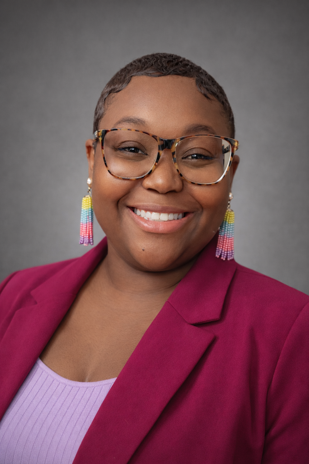Man in a blue shirt standing outdoors, smiling. Background features greenery, fence.