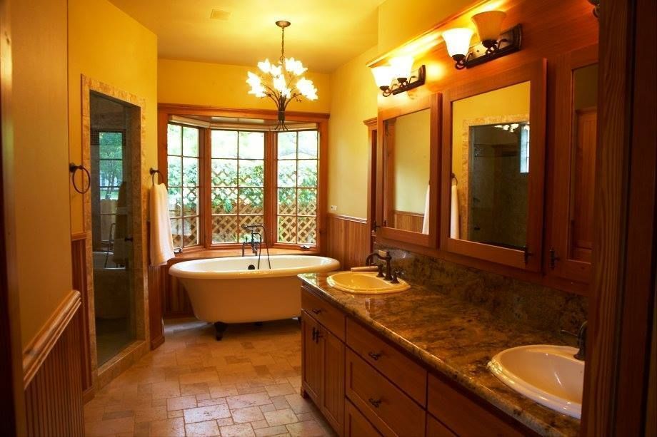 Warm-lit bathroom with clawfoot tub, double sink vanity, and large windows.