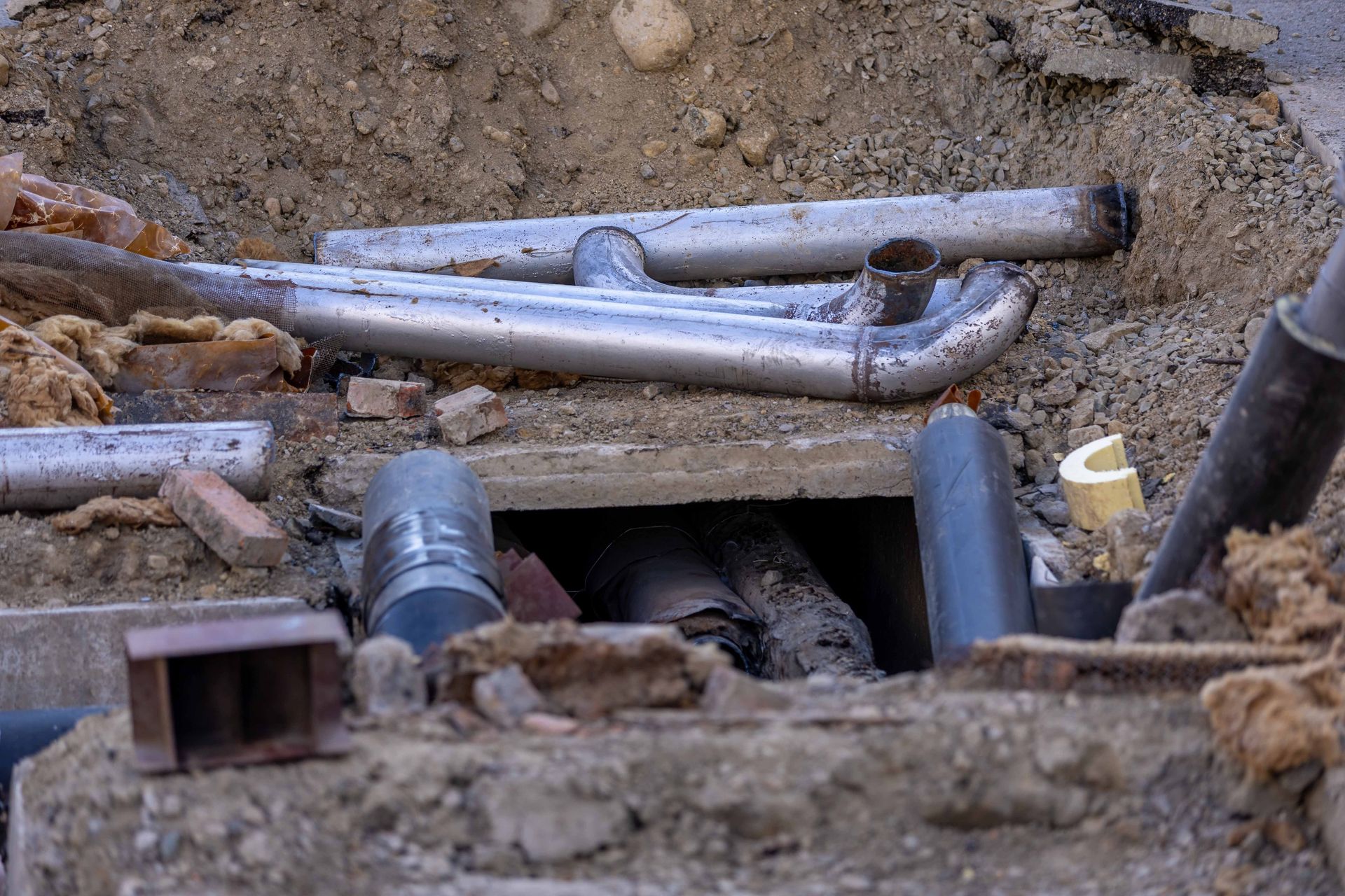 A trench with exposed pipes and a utility box in dirt, showing underground repair work.