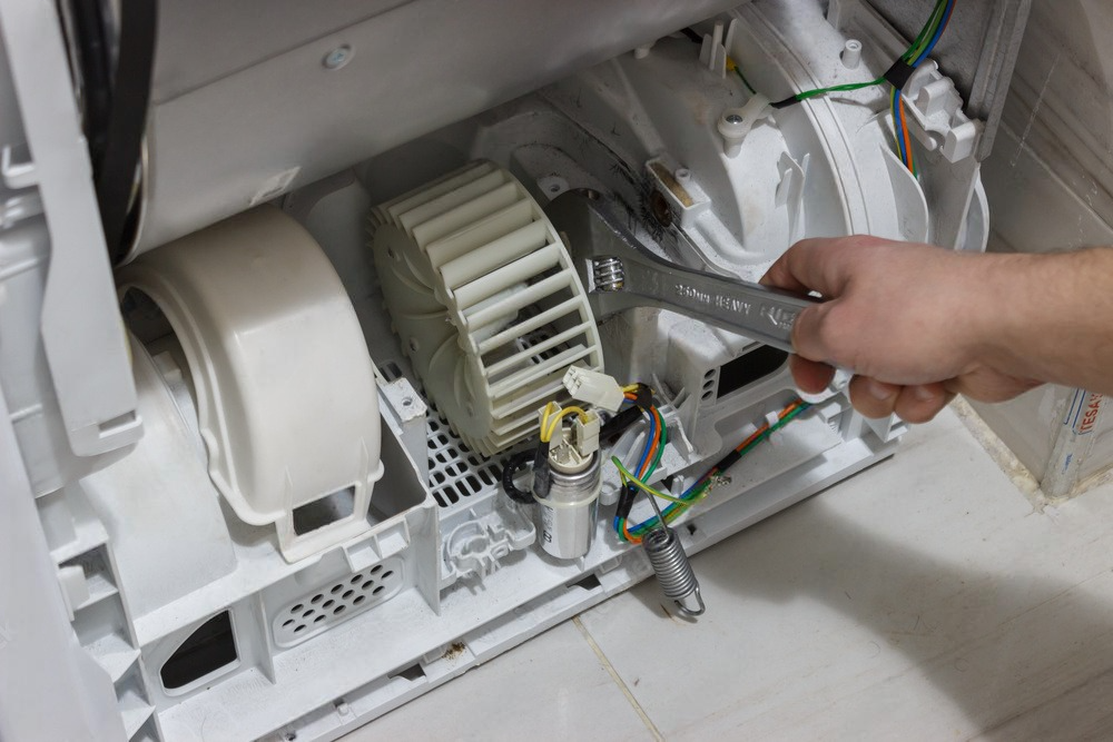 A person is fixing a washing machine with a wrench.