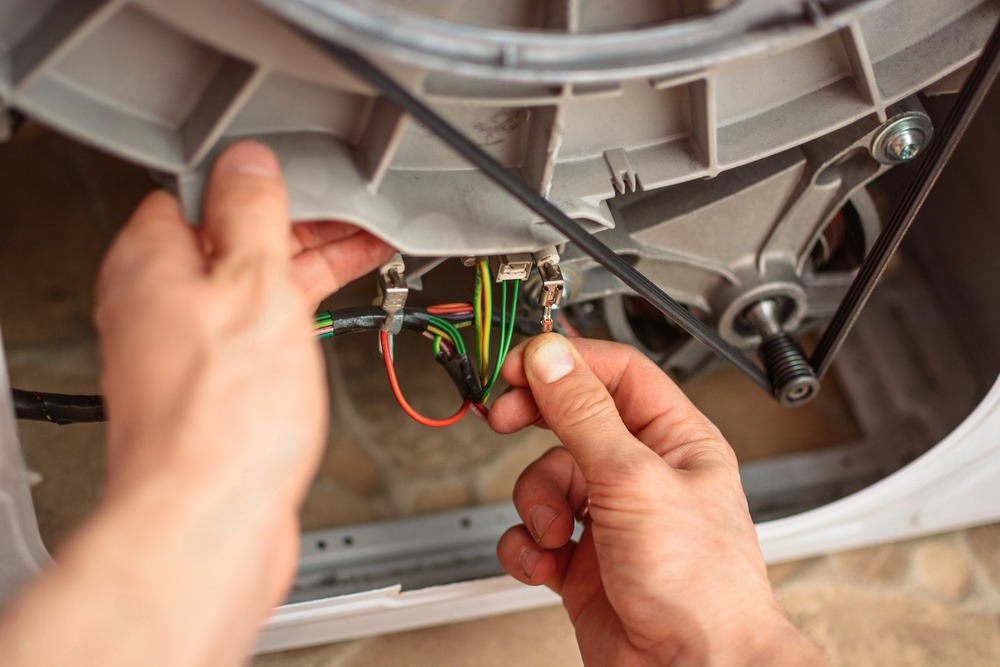 A person is fixing a washing machine with a screwdriver.