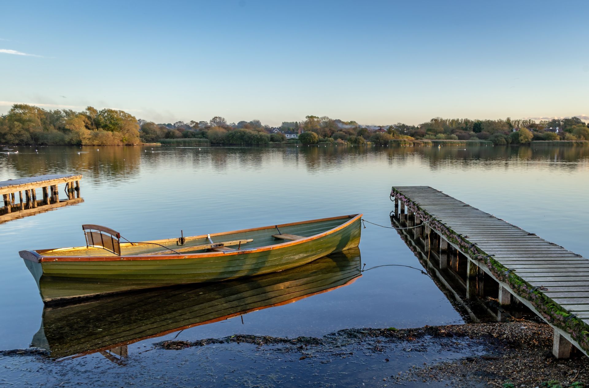 A weathered green rowboat on calm water between two wooden docks, reflecting the sunlight.