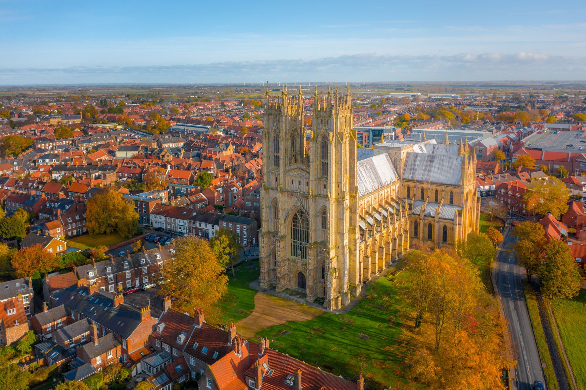 Aerial view of a large gothic cathedral in a town with red-roofed buildings and fall foliage.