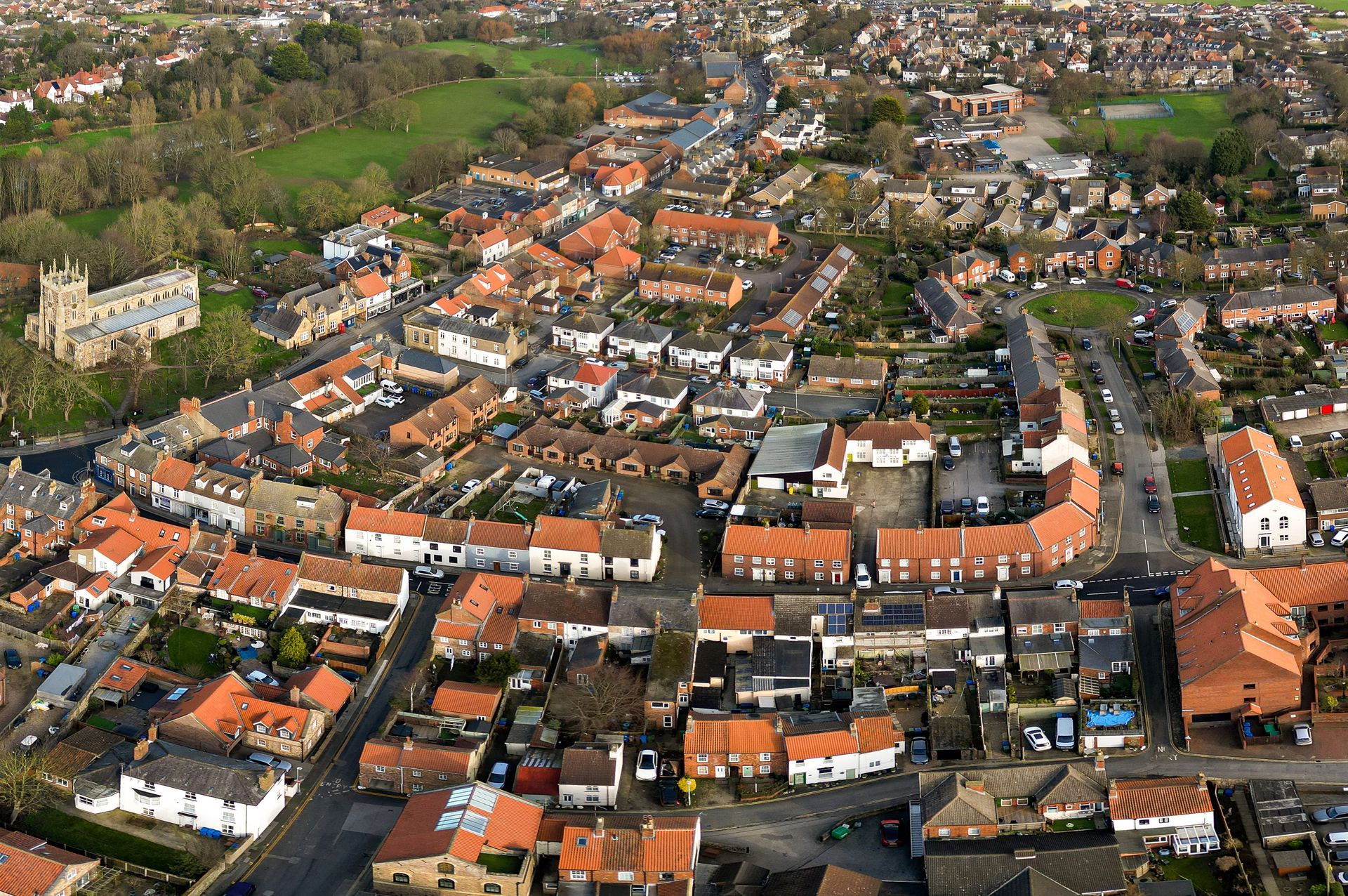 Aerial view of a small town with red-tiled roofs, a church, and green spaces.