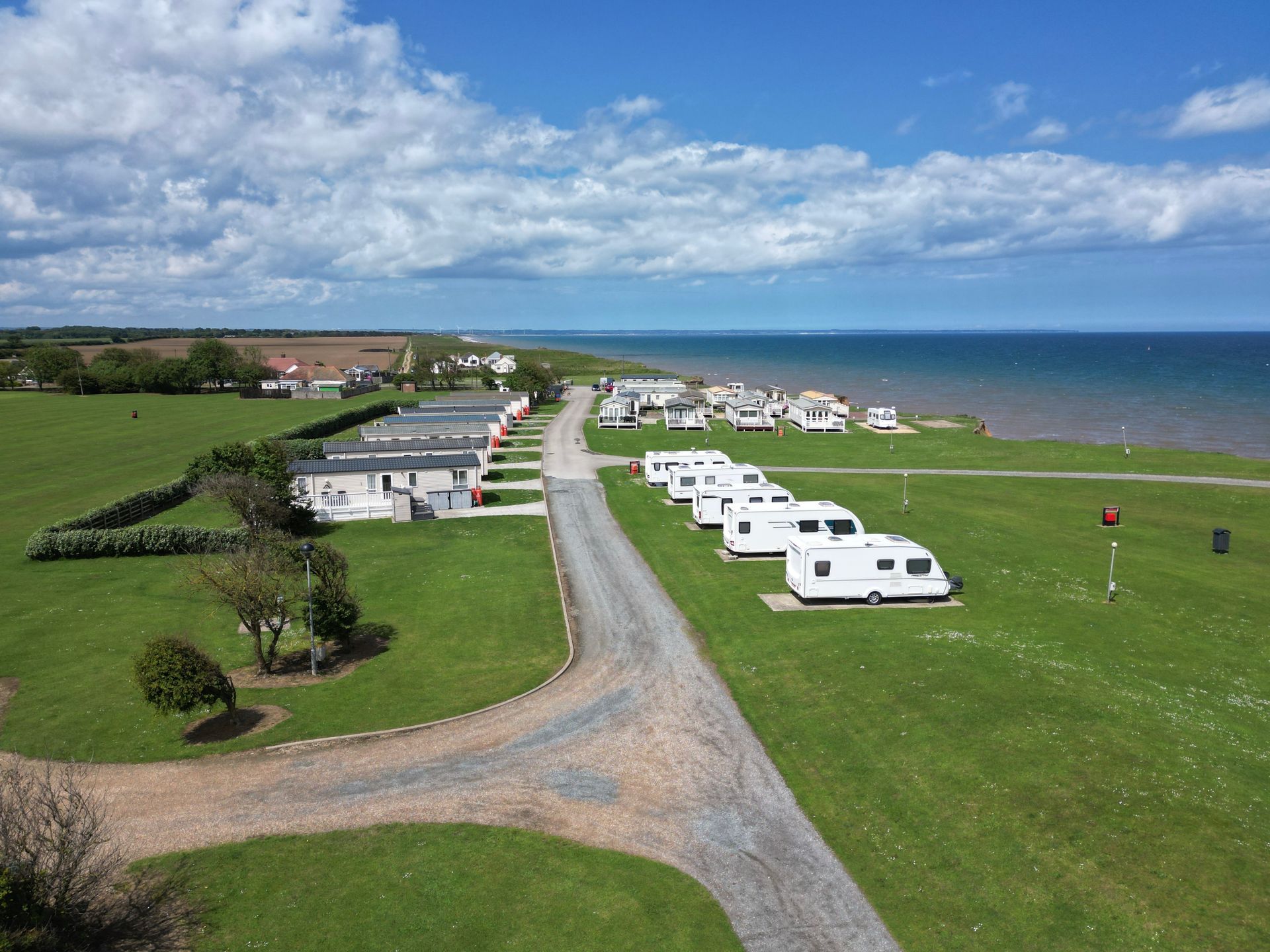 A caravan park on a grassy coast with a road, trailers, the sea, and a blue sky.