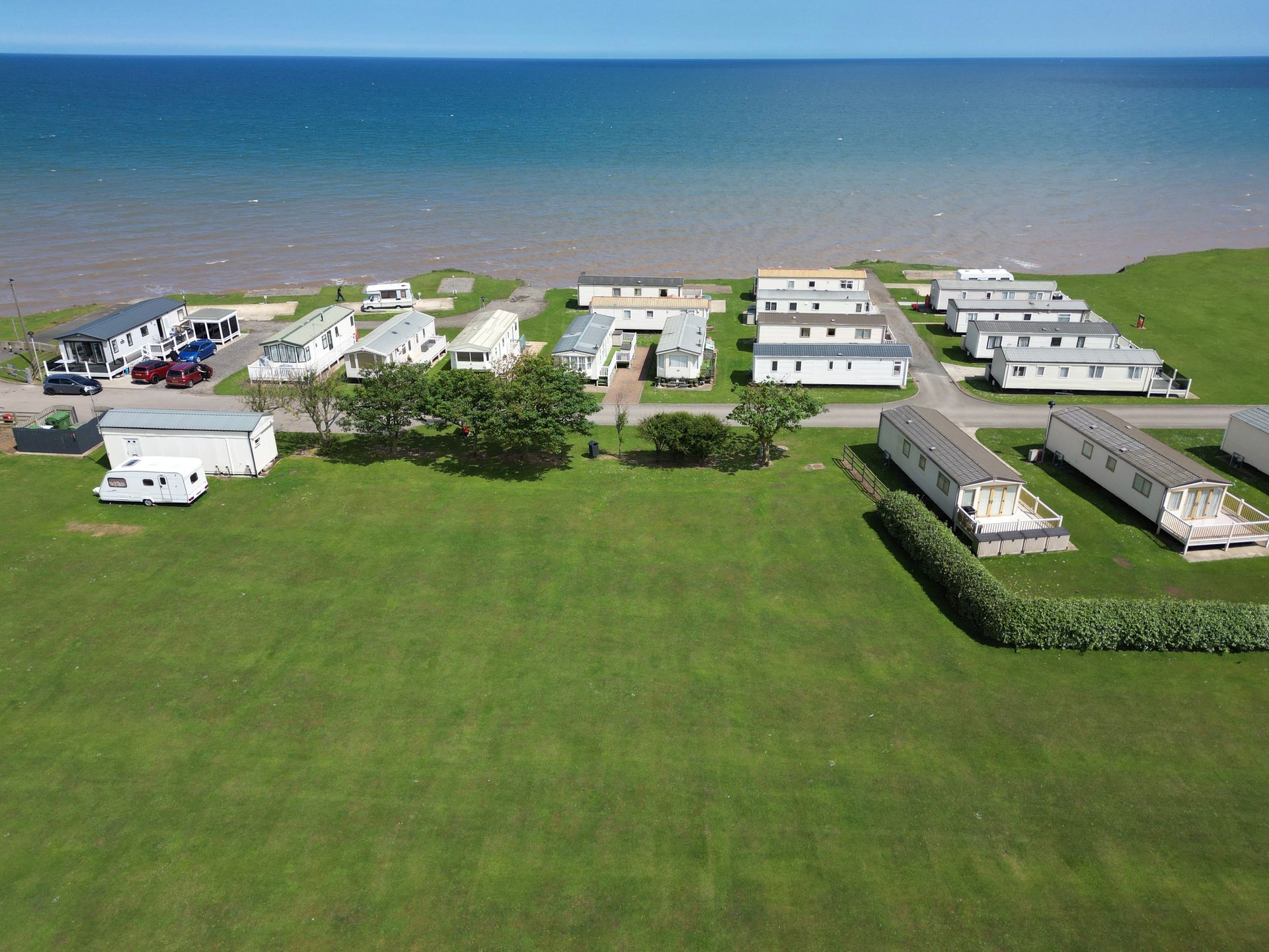 Aerial view: Static caravans on green grass near the sea on a sunny day.