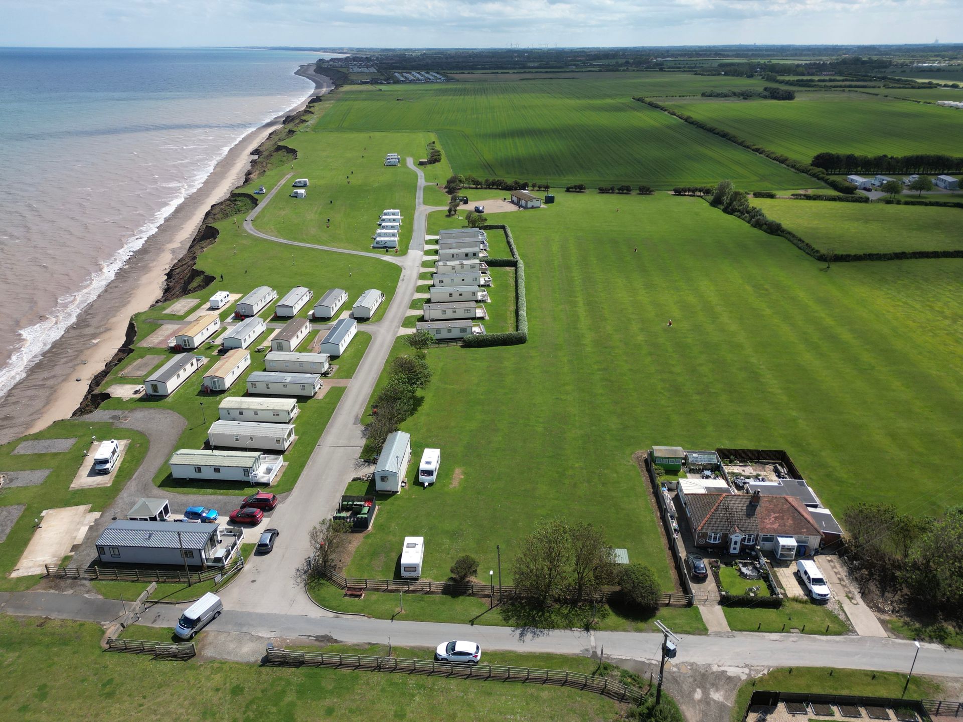 Aerial view of a caravan park next to a coastline, green fields, and a clear sky.