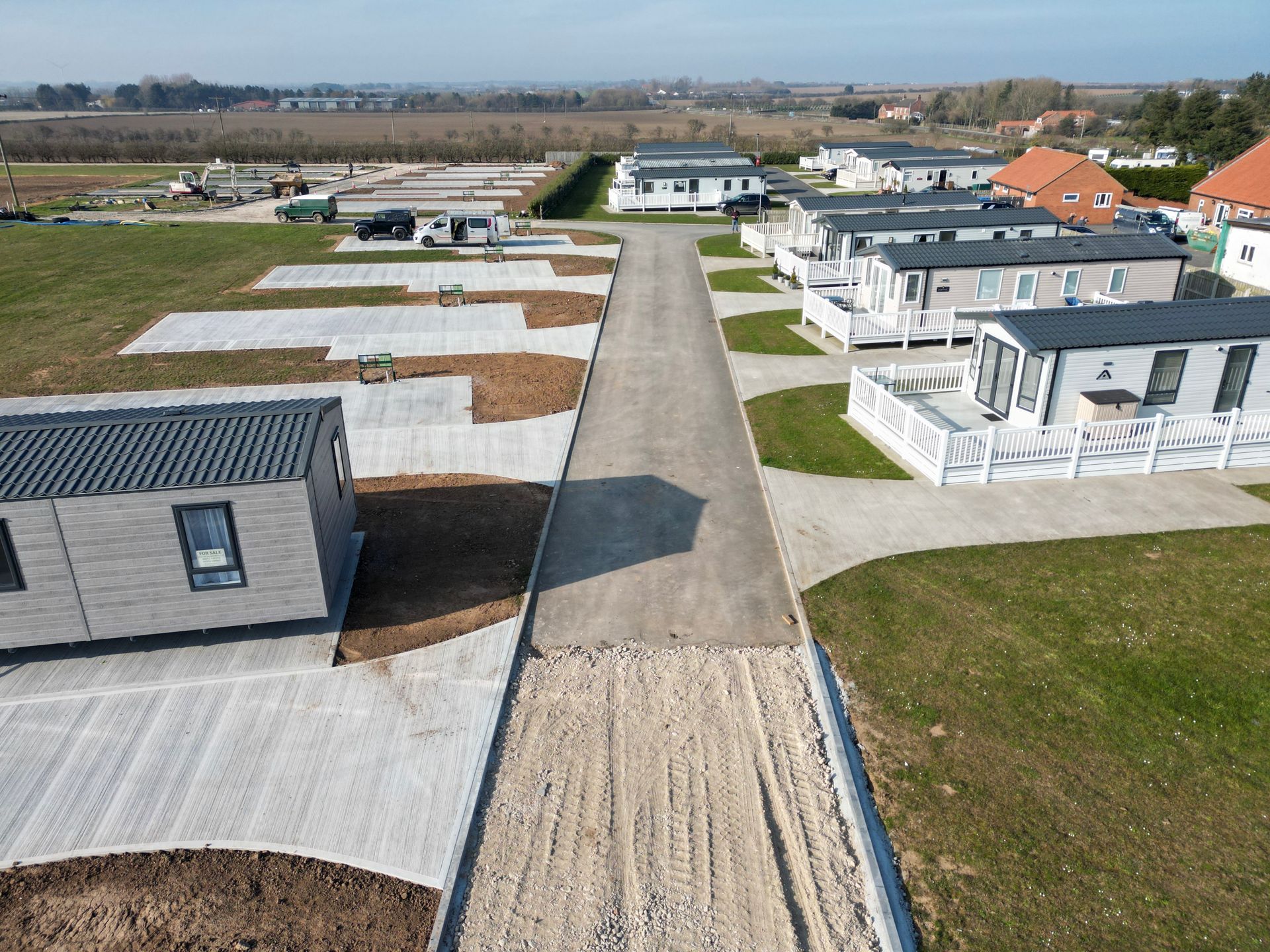 Aerial view of a caravan park with rows of gray caravans, road, and gravel areas.