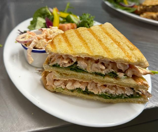 Grilled sandwich with pink filling, side of coleslaw and salad on a white plate.