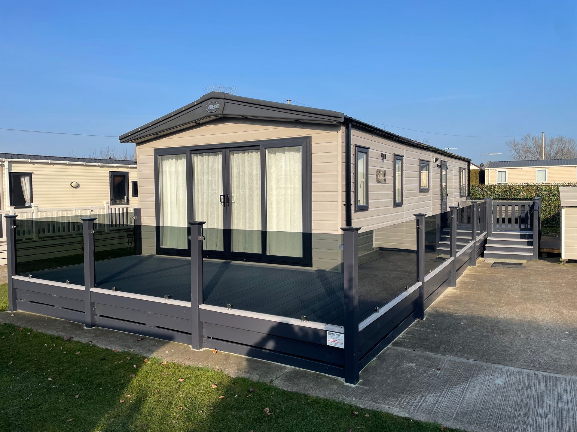Mobile home with gray deck and railings in a sunny outdoor setting.