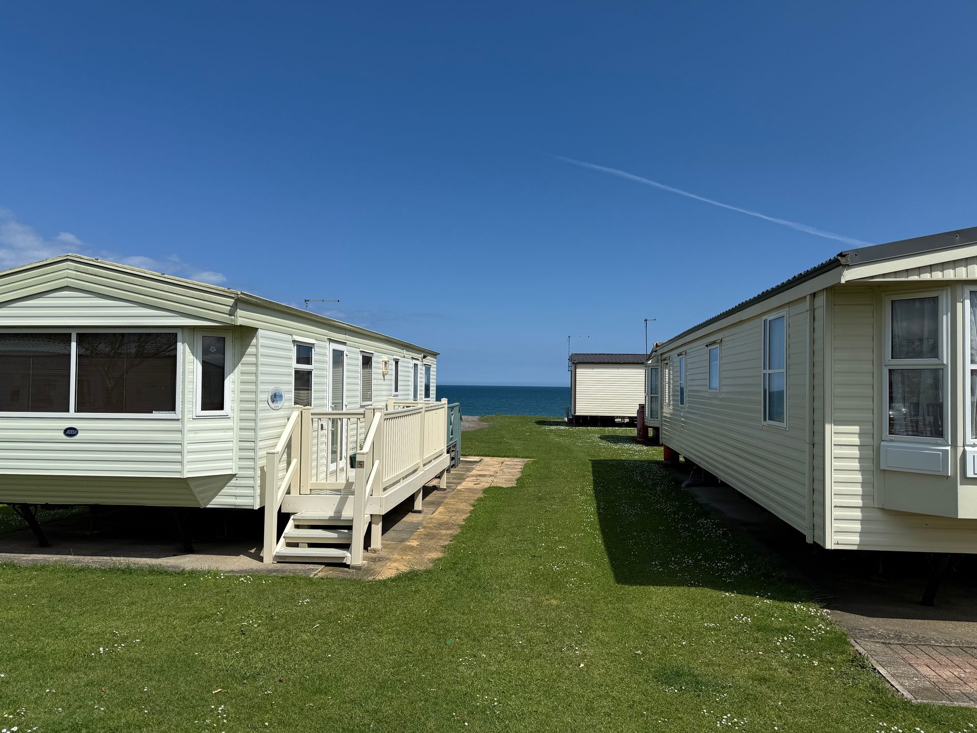 Two white caravans on a grassy lot, blue sky and sea in the background.