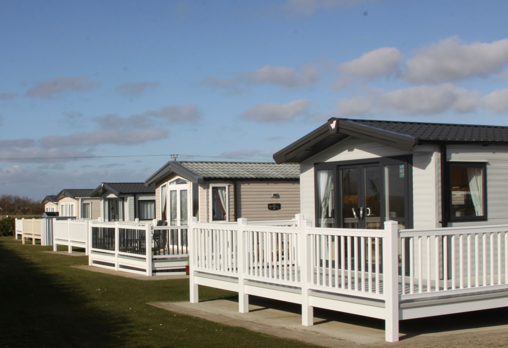 Row of holiday caravans with white railings, under a blue sky with fluffy clouds.