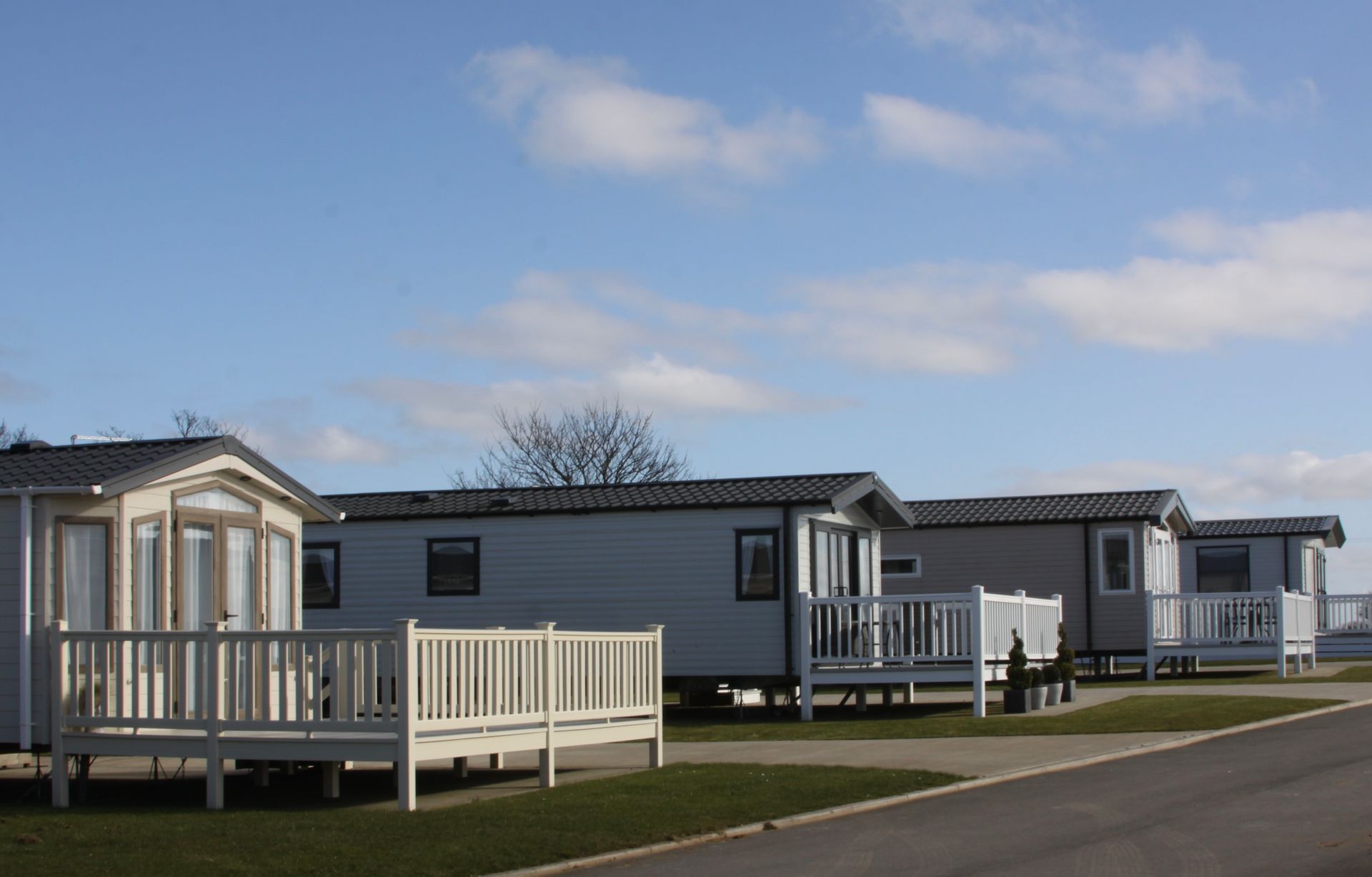 Row of static caravans with white decks on a sunny day, grass and road in the foreground.