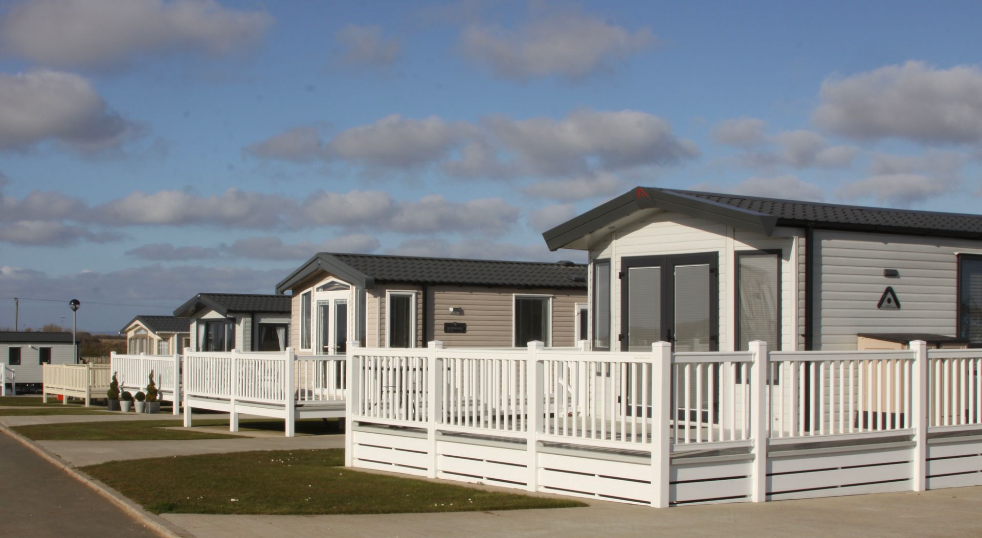 Row of modern gray and white caravans with white railings on a sunny day with blue sky and clouds.
