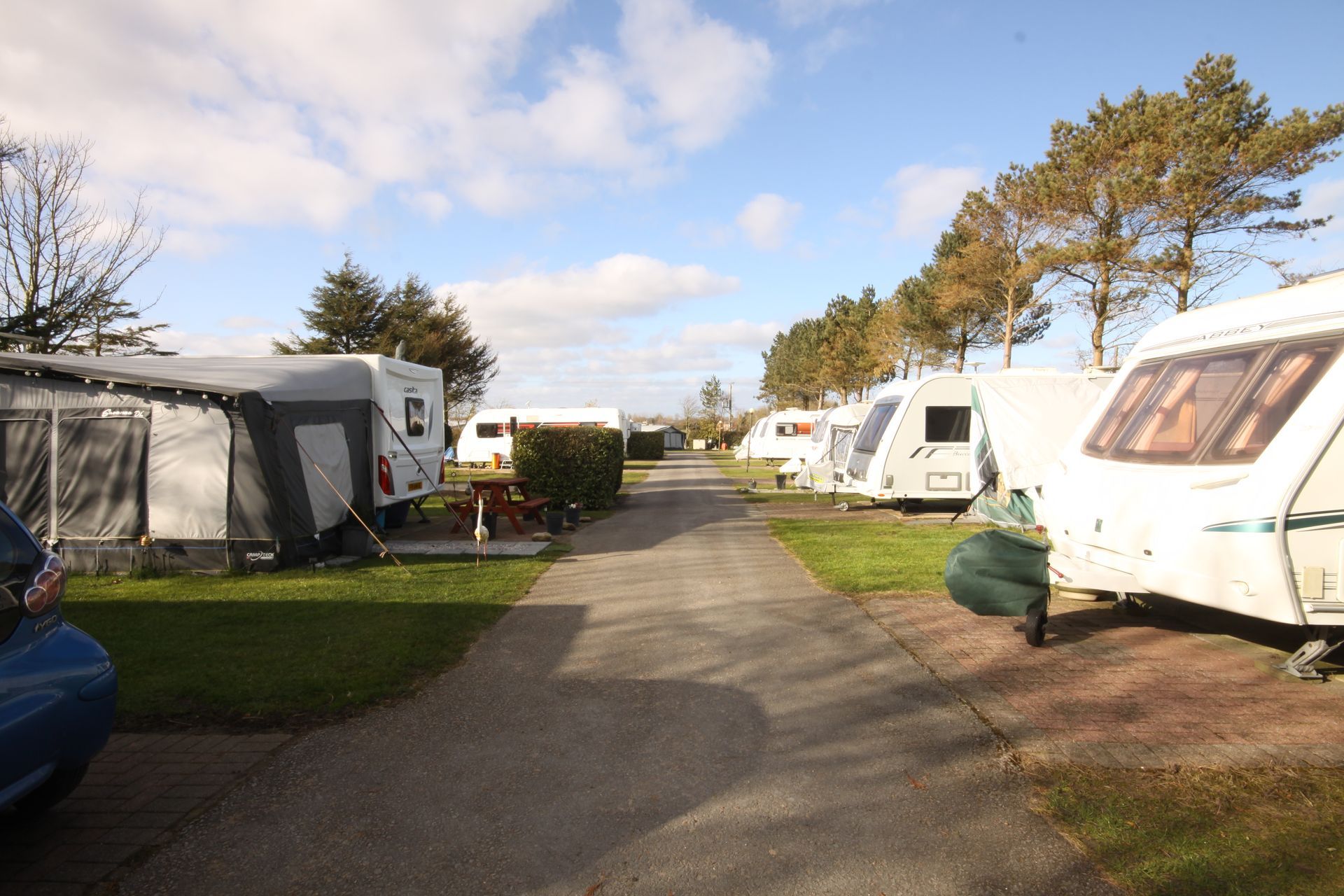 A row of caravans parked on a paved road at a campsite, under a cloudy sky.