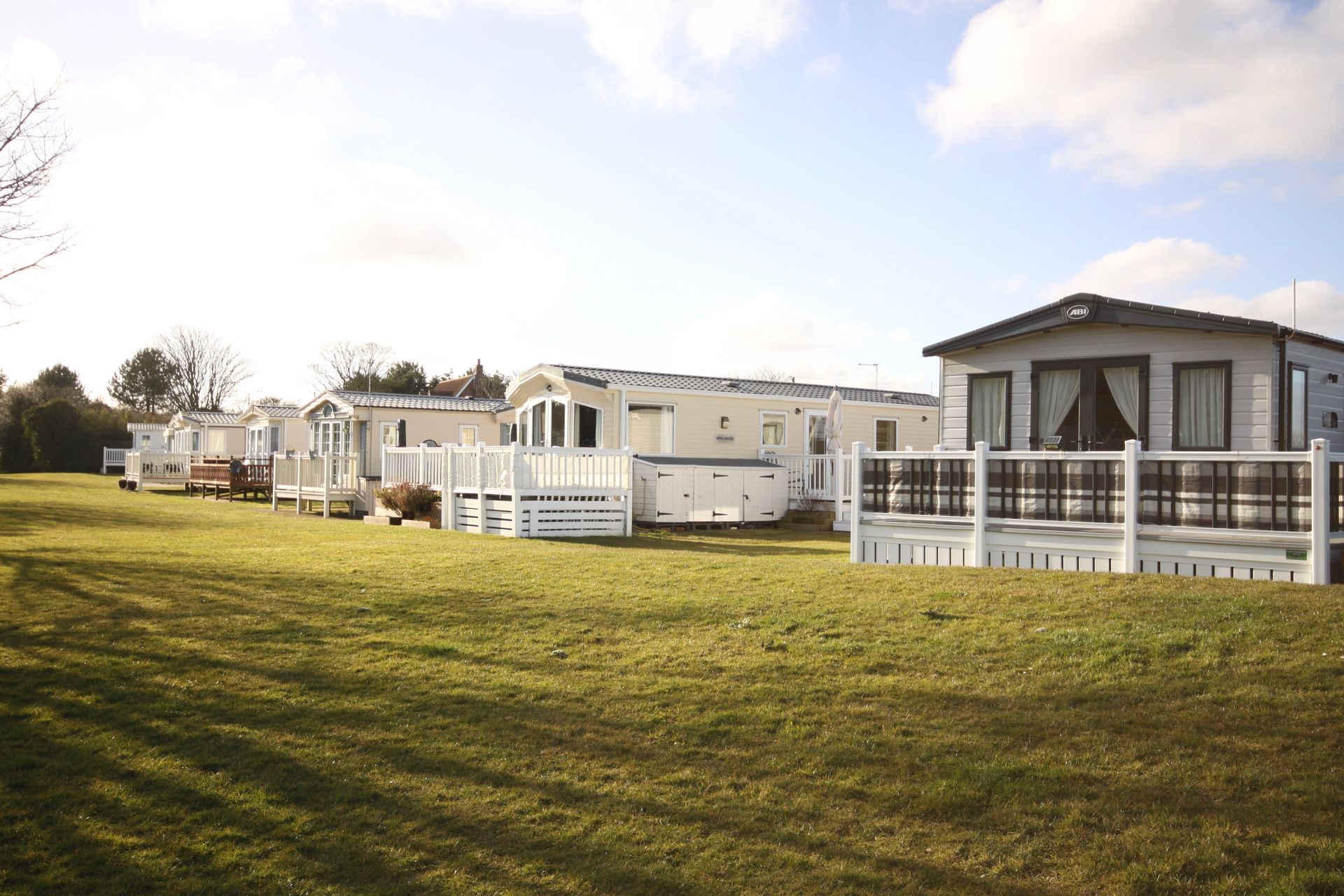 Row of white mobile homes on green grassy field under sunny sky.