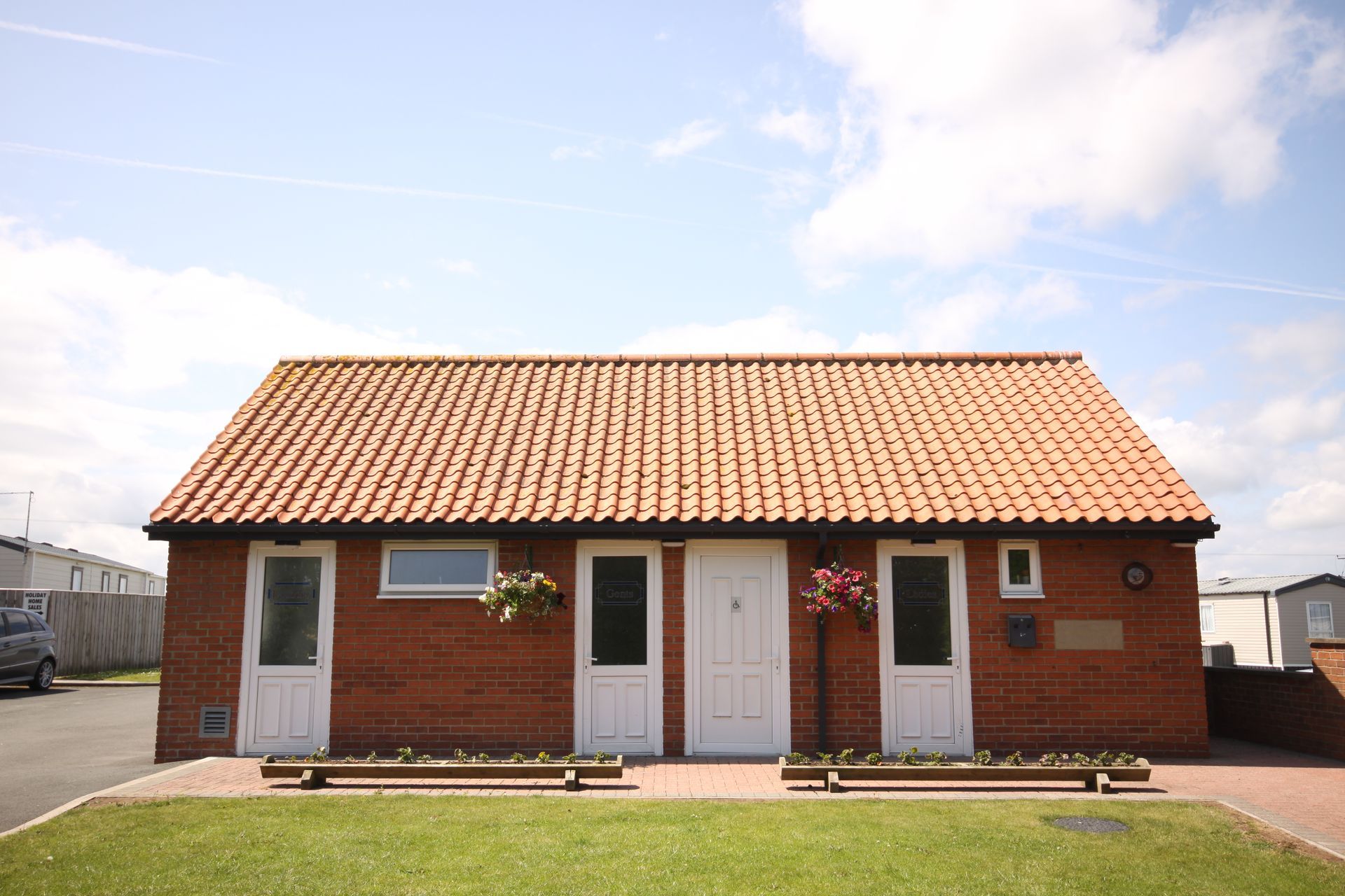 Brick building with terracotta roof, white doors, and flower boxes, under a partly cloudy sky.