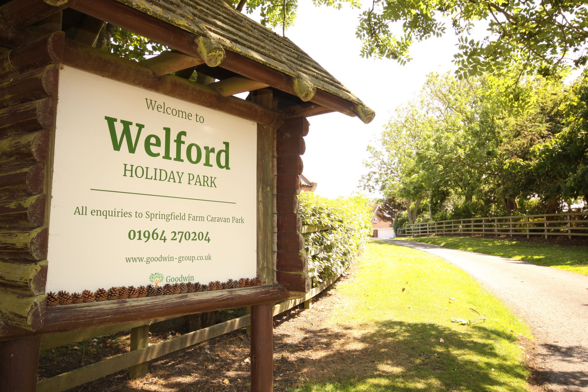 Sign for Welford Holiday Park, wooden structure, entrance path, green surroundings.
