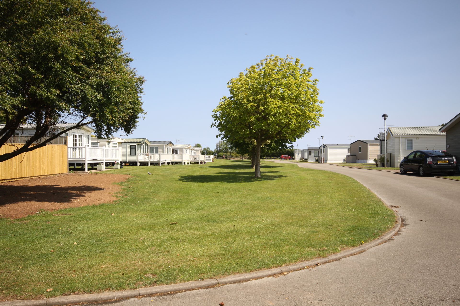 A row of white mobile homes on a green lawn with trees on a sunny day.