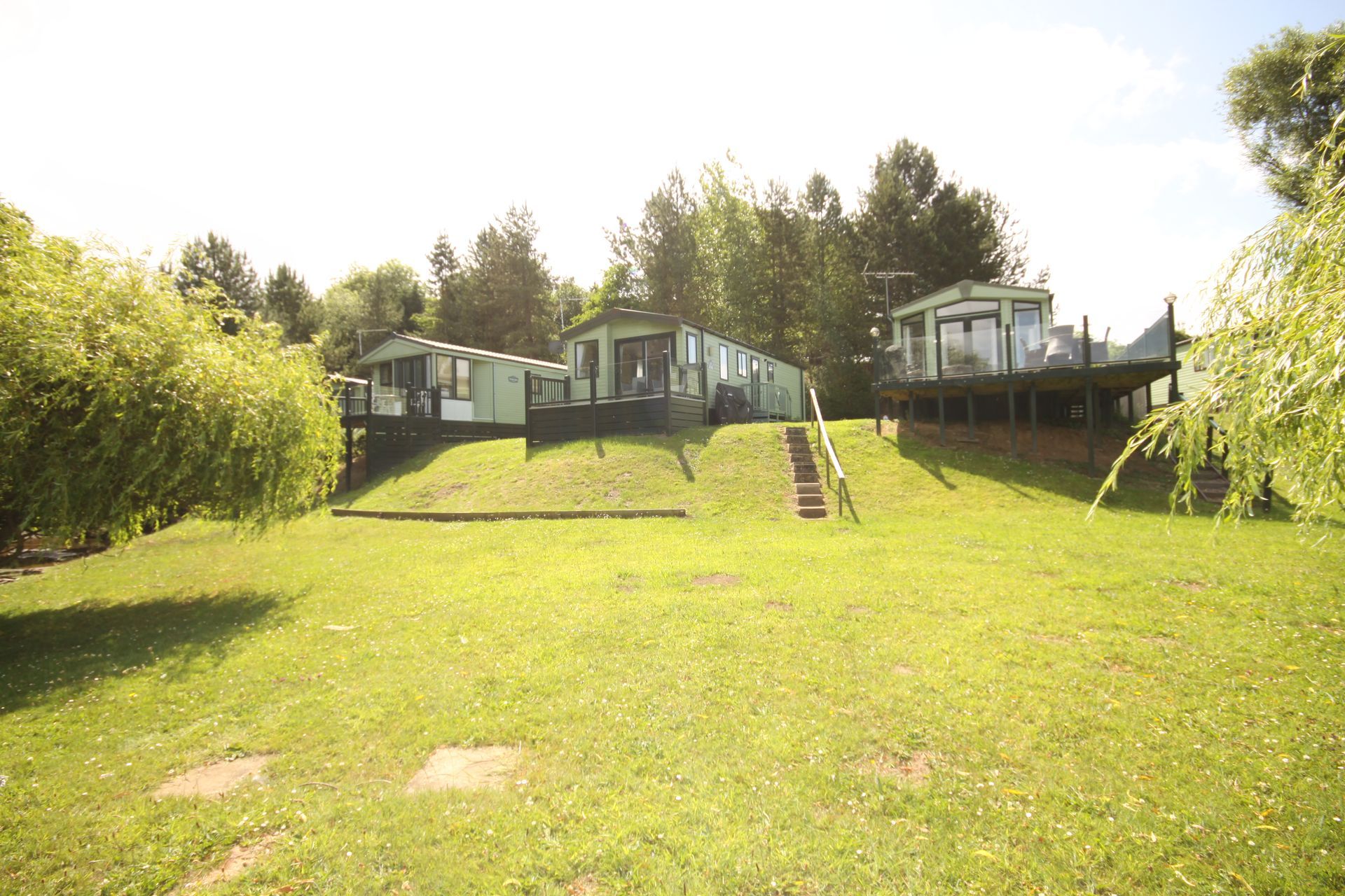 Three mobile homes on a grassy hillside with trees. Sunny day.
