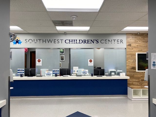 The reception desk of Southwest Children’s Center, featuring a blue base, glass partitions, and a wooden accent wall.