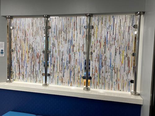 A decorative privacy screen with vertical, multicolored paper-like strips held by four chrome metal poles on a shelf.