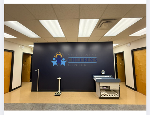 Interior of a children's center waiting area with a dark blue feature wall, medical scale, and exam table.