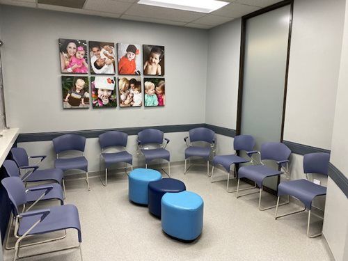 Waiting area with blue chairs arranged in a semi-circle, three blue stools in the center, and wall-mounted photo canvases.