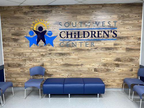 Waiting room at Southwest Children’s Center with blue chairs and a logo on a rustic wood-look wall.