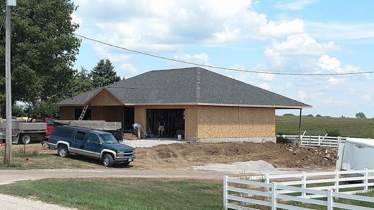 A blue truck is parked in front of a house under construction.
