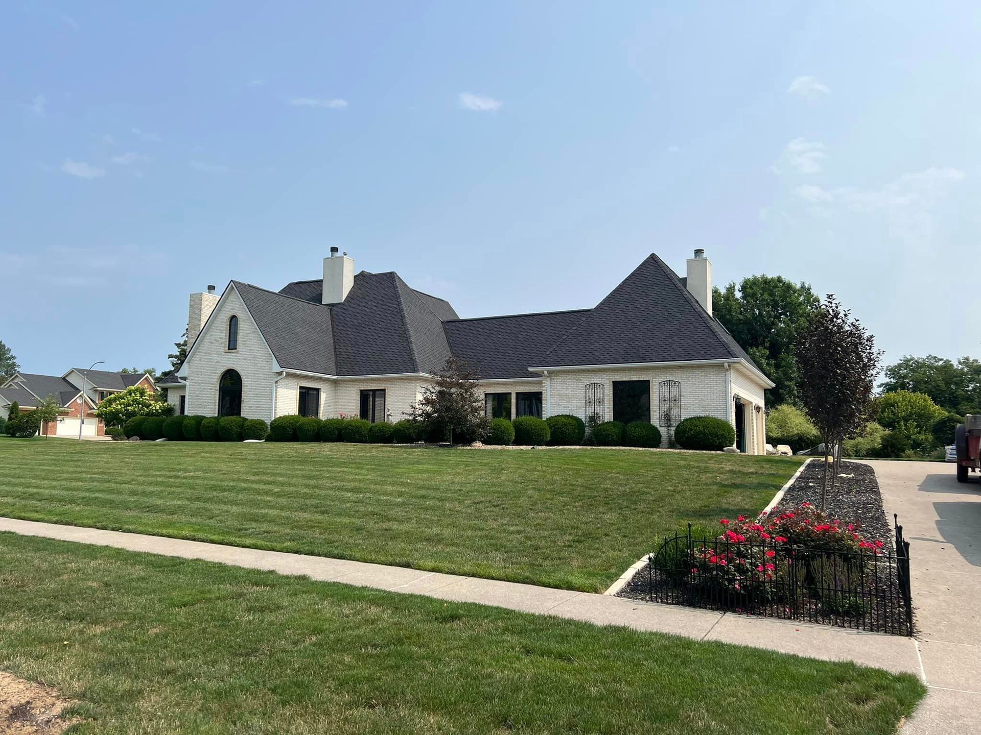 A large white house with a black roof is sitting on top of a lush green lawn.