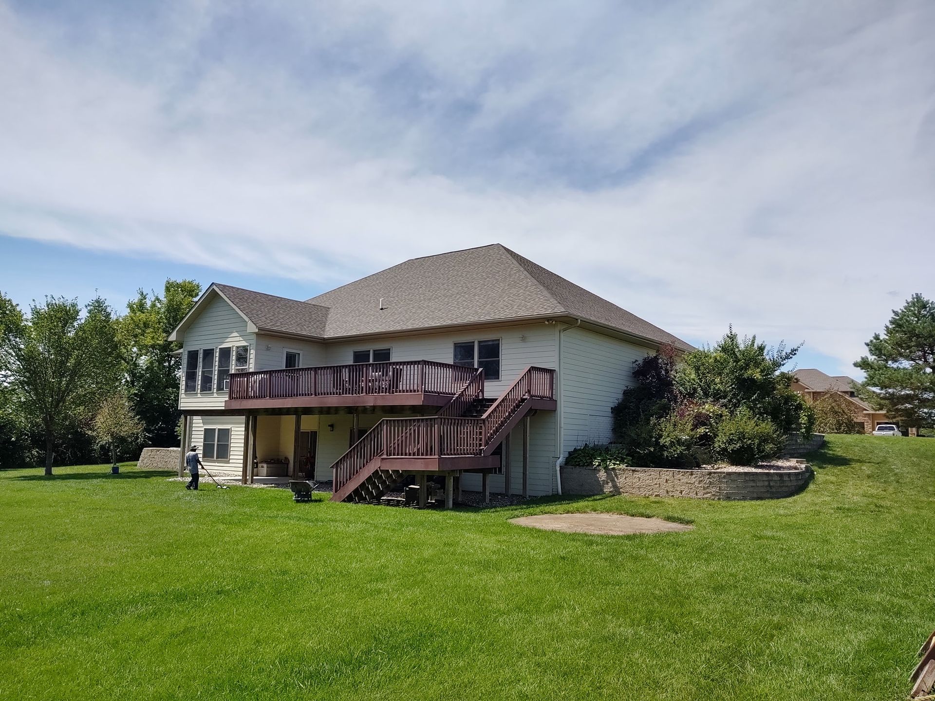 A large house with a large deck and stairs is sitting on top of a lush green field.