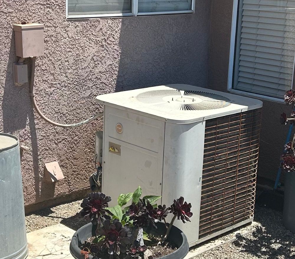 An outdoor air conditioning unit next to a wall, with a flower pot in the foreground.