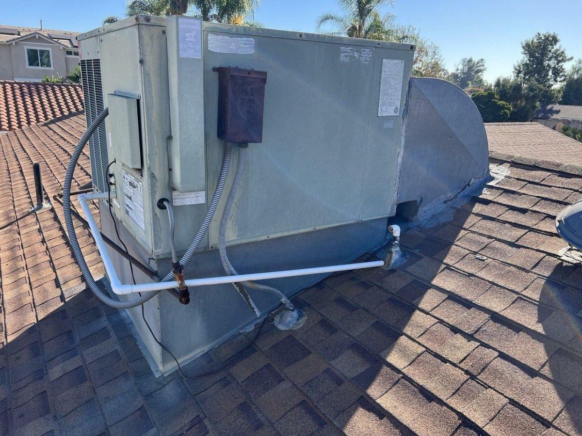 Rooftop HVAC unit on a tiled roof. Metal components, pipes, and vents visible in daylight.