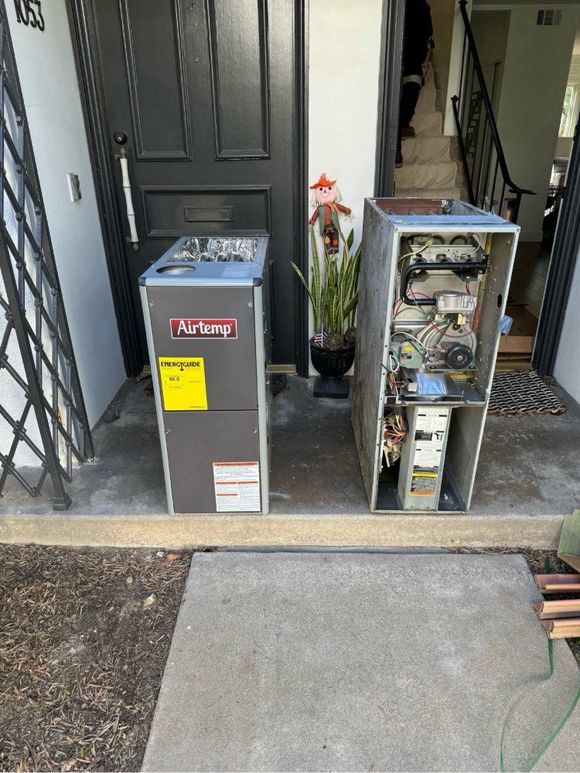 Two HVAC units, one new and enclosed, one old and open, outside a door.