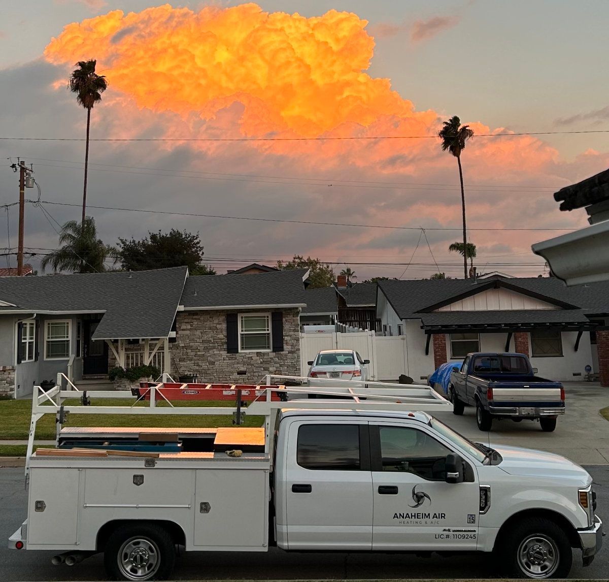 White truck parked on a street in front of houses with a fiery orange and yellow cloud in the sky.