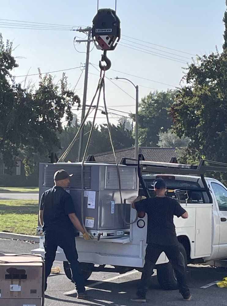Two workers loading equipment onto a truck with a crane. Sunny outdoors.